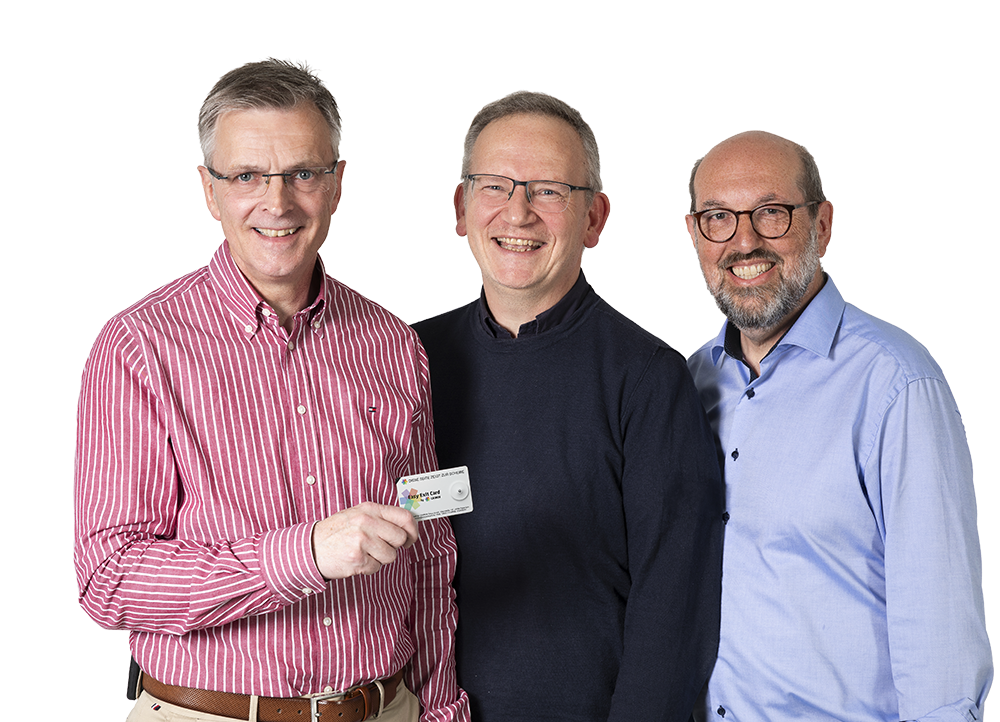 Drei lächelnde Männer mittleren Alters in Hemden; der linke hält eine kleine Karte vor sich.