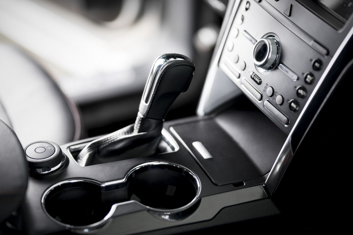 Auto-Innenraum mit schwarzem Automatikschalthebel, zwei Getränkehaltern und mittlerer Bedienkonsole mit Drehknopf und Tasten
