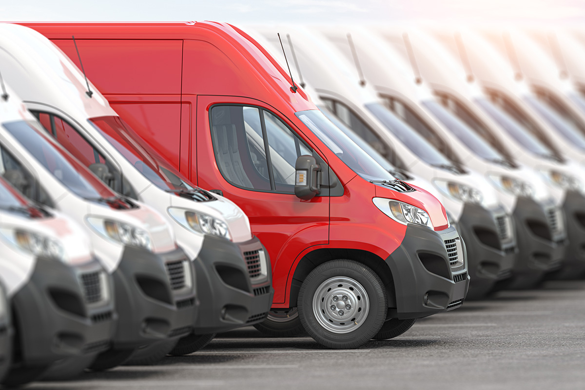 Reihe geparkter Lieferwagen in einem Hof, ein roter Transporter sticht in einer Linie weißer Fahrzeuge hervor.